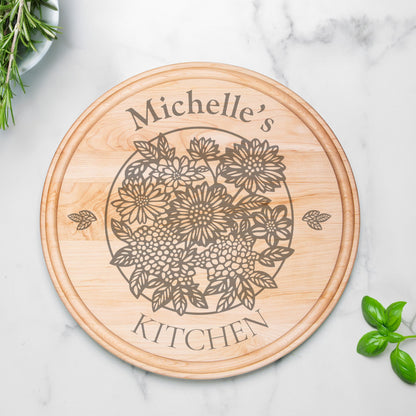 Round maple wood serving board with groove, etched with a floral design and personalized text, "Michelle's Kitchen" on a marble countertop