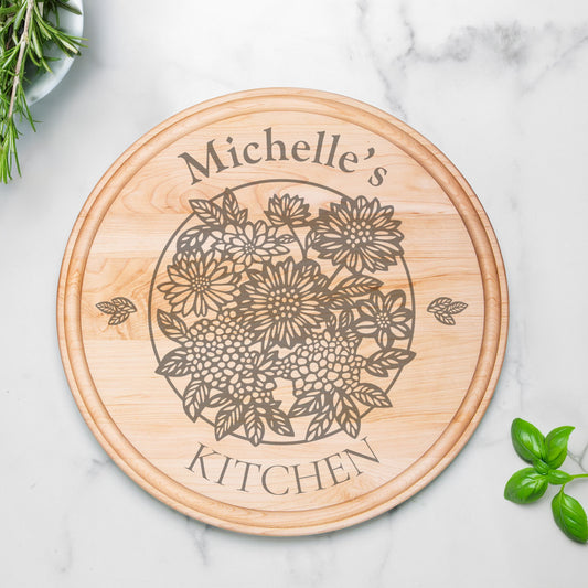 Round maple wood serving board with groove, etched with a floral design and personalized text, "Michelle's Kitchen" on a marble countertop